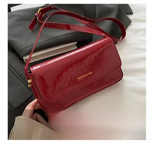 Close-up of glossy wine red patent leather shoulder bag with gold hardware details