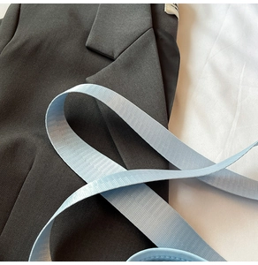 Détail du col d'un blazer gris foncé avec une sangle tissée bleu clair sur tissu blanc
