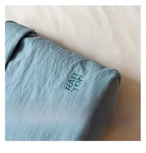 Close-up of light blue oxford fabric texture with premium RAH TOP letter embroidery