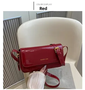 Detail of red patent leather shoulder bag with gold brand logo and adjustable strap