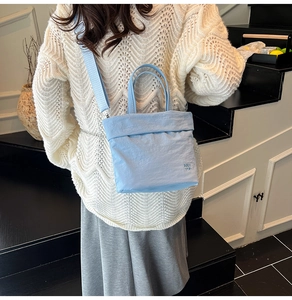Détail du sac bandoulière bleu clair avec doubles poignées et broderie de marque