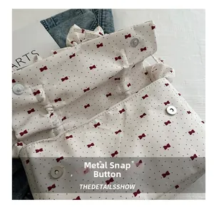 Detail of silver magnetic snap closure on white pleated bag with red bow print