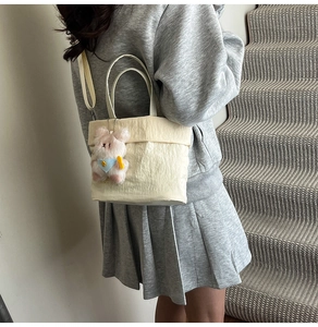 Détail du sac bandoulière plissé beige avec breloque ours rose porté par un mannequin