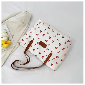 Detail van de witte tote bag met kersenprint, bruine leren riemen en gouden klinknagels