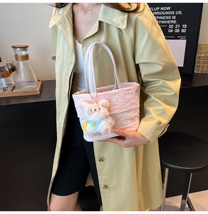 Détail d'un sac à main plissé rose avec logo et breloque ours en peluche blanc sur mannequin