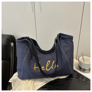 Gros plan de la broderie Hello jaune sur un sac cabas en denim bleu foncé avec cuir