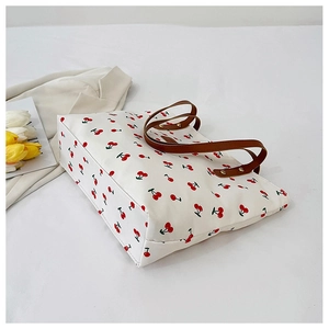 Detail van de witte canvas draagtas met kersenprint en bruine leren hengsels met klinknagels