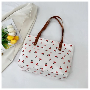 Detailed view of white cherry print tote bag with brown leather straps and gold rivets