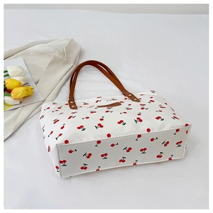 Detail van de tote bag met kersenprint, bruine leren hengsels en merklogo op wit