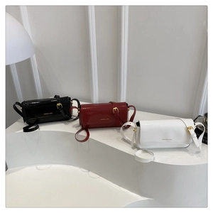 Close-up of three patent leather mini flap crossbody bags in black, burgundy, and white