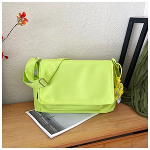 Detalle del bolso bandolera verde neón de tela Oxford con colgante de flor amarilla en mesa