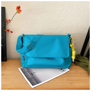 Detalle de bolso mensajero de nailon azul con amuleto de peluche amarillo en mesa