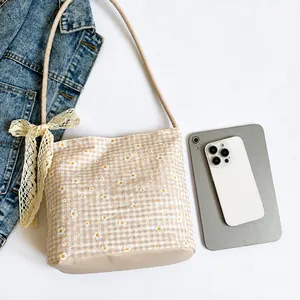 Dettaglio del ricamo a margherite e fiocco di pizzo su borsa tote beige a quadretti con scala