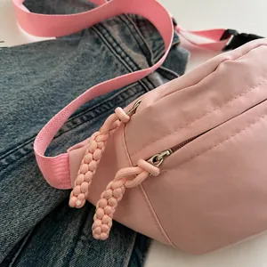 Detailopname van de roze crossbodytas met dubbele ritssluiting en geweven koordtrekkers