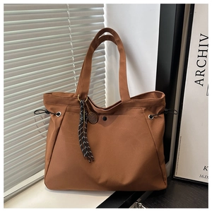 Detail of brown pleated tote bag with drawstring features and a tennis racket charm