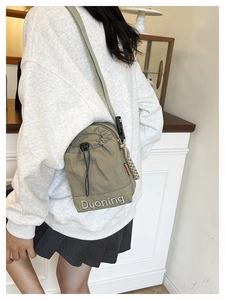 Détail du sac bandoulière en nylon vert gris avec cordon de serrage et logo brodé