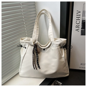 Detail of white nylon tote bag featuring side drawstrings and a woven pendant on a windowsill