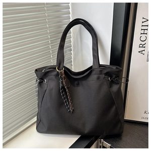 Detailed close-up of a black nylon tote bag featuring side drawstrings and woven rope charm