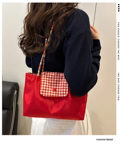 Dettaglio borsa a spalla in nylon rosso con patta a scacchi e tracolla intrecciata