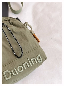 Détail du sac à cordon en nylon vert avec broderie Duoning et étiquette orange fashion