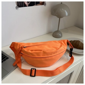 Detail of a bright orange nylon crossbody bag with dual zippers on a minimalist desk