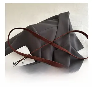 Détail d'une bandoulière en daim marron avec coutures précises sur un blazer gris
