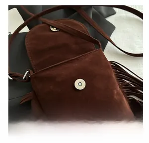 Détail du sac en daim marron foncé avec boucle magnétique ronde en métal et franges