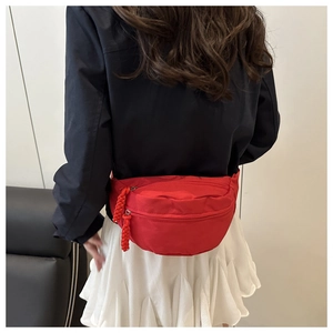 Detail shot of a red nylon crossbody bag featuring double zippers and woven rope pullers