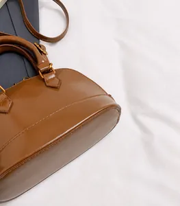 Detail of a brown leather shell handbag with round handle and metallic hardware
