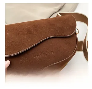 Nahaufnahme braune Wildleder-Satteltasche mit Fashion-Schriftzug und breitem Gurt