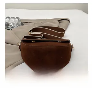 Nahaufnahme der braunen Wildleder-Satteltasche mit breitem Gurt auf grauem Stoffhintergrund