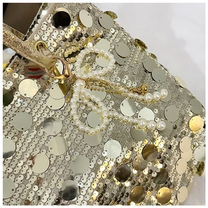 Detailed close-up of golden sequins and a pearl bow charm on a stylish shoulder bag