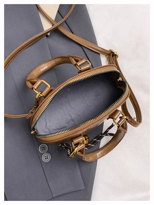 Detailopname van de bruine mini-tas met grijze voering en goudkleurige metalen accenten