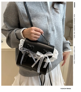 Détail d'un sac bandoulière en cuir noir avec bordure en dentelle et nœud à carreaux