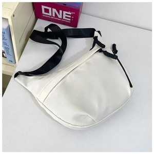 Close-up van witte nylon halvemaantas met zwarte verstelbare riem en geweven ritsdetail