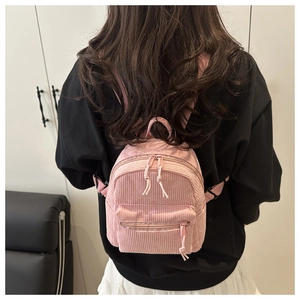 Pink corduroy mini backpack detail showing soft ribbed texture on a model outdoors