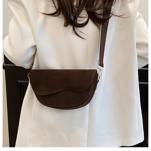 Detail einer dunkelbraunen Satteltasche mit Wellenkanten-Design auf weißem Blazer