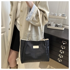 Detailed view of black quilted tote bag featuring metal chain strap and logo plaque