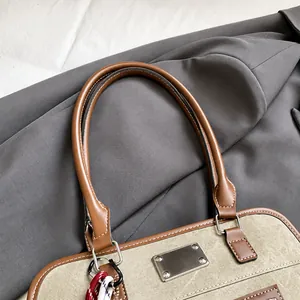 Detail des braunen Ledergriffs mit weißen Nähten auf der grünen Canvas-Handtasche