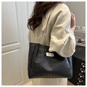 Detail of black quilted tote bag with silver chain strap worn over the shoulder by a model