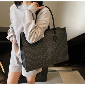 Detail of black tote bag with gray M letter pattern and golden hardware accents