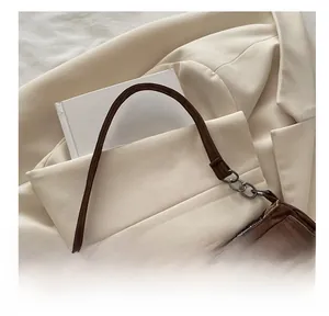 Detail van bruine suède tas met zilveren gespen en kettingriem op witte blazer