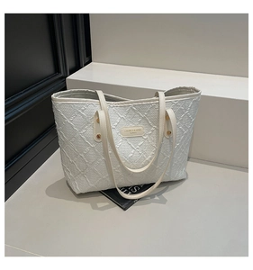 Detailed view of white tote bag with textured quilted pattern and cream leather brand tag