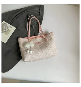 Detail of beige quilted tote bag with pink leather strap and plush cloud charm accent