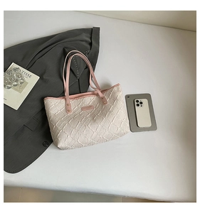 Detail of quilted beige tote bag with pink handles and golden rivets on white surface