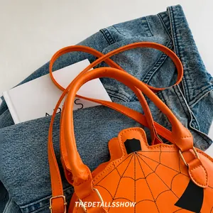 Detail of orange pumpkin crossbody bag with black spider web pattern and leather strap