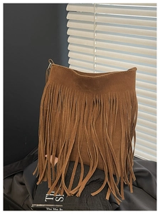 Detail of a brown suede bucket bag with long tassels and metallic hardware accents