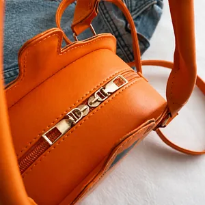 Macro shot of smooth gold double zippers on a pumpkin-shaped orange crossbody bag