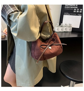 Close-up of deep brown suede tote bag with decorative bow and silver heart pendant