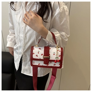 Λεπτομέρεια της μοντέρνας τσάντας με τύπωμα κεράσι και φαρδύ ιμάντα ώμου με μενταγιόν